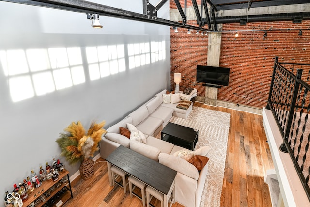 living room featuring hardwood / wood-style flooring, brick wall, a high ceiling, and stairway