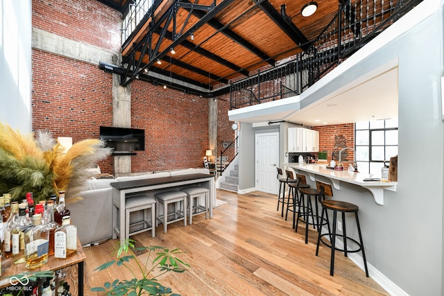 kitchen featuring light wood-style floors, brick wall, white cabinets, and a high ceiling