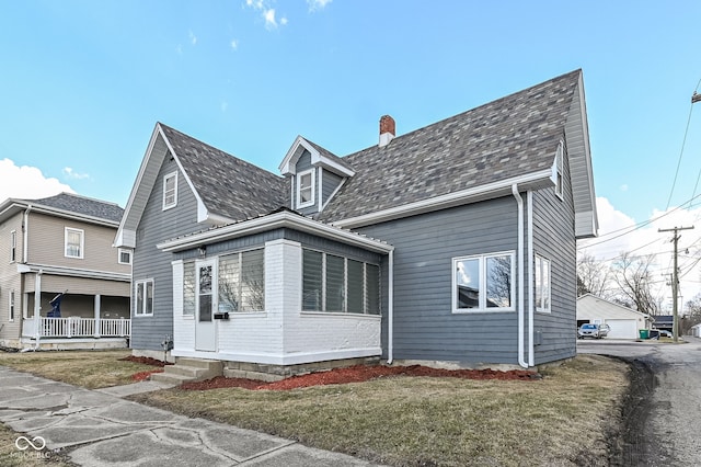 view of front of property featuring an outbuilding, a front lawn, roof with shingles, and a garage