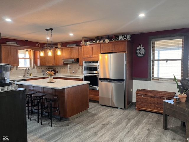 kitchen with stainless steel appliances, light countertops, brown cabinetry, a sink, and under cabinet range hood