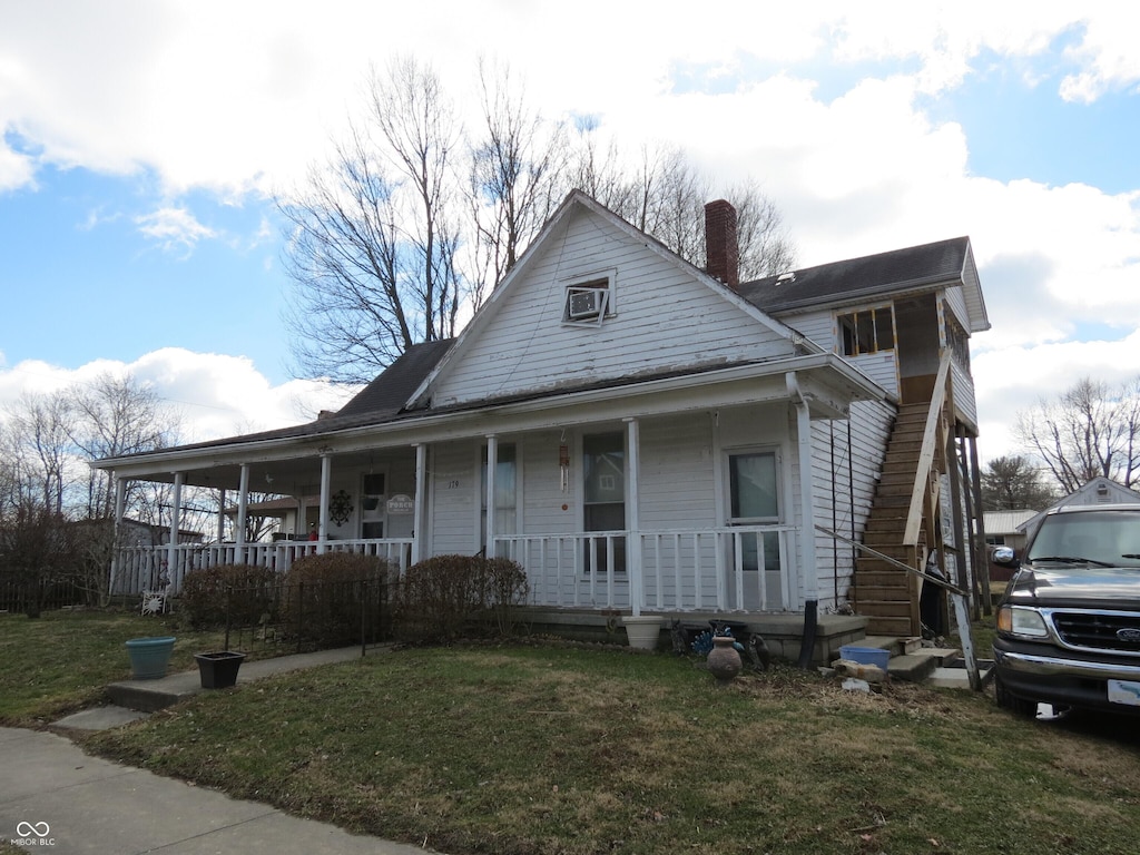 view of front of home featuring covered porch, a front lawn, and a chimney