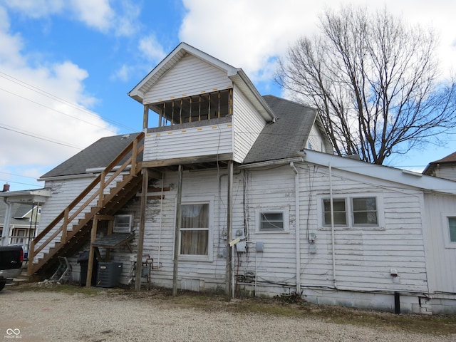 rear view of property with a shingled roof, stairway, and central AC unit