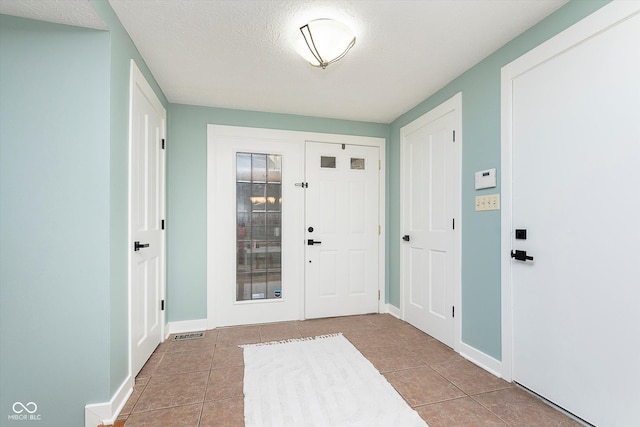 foyer with visible vents, a textured ceiling, baseboards, and tile patterned floors