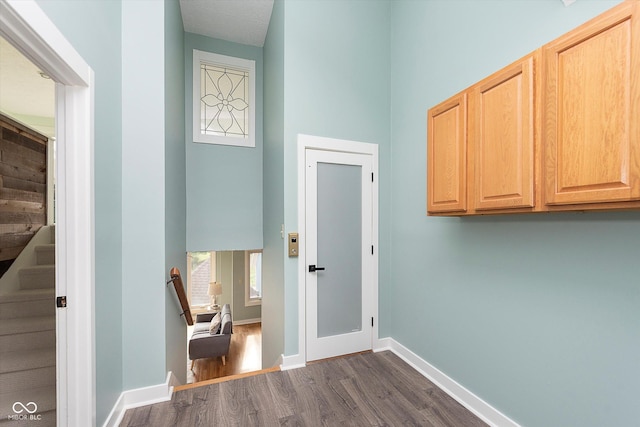 hall featuring a towering ceiling, stairs, baseboards, and dark wood finished floors