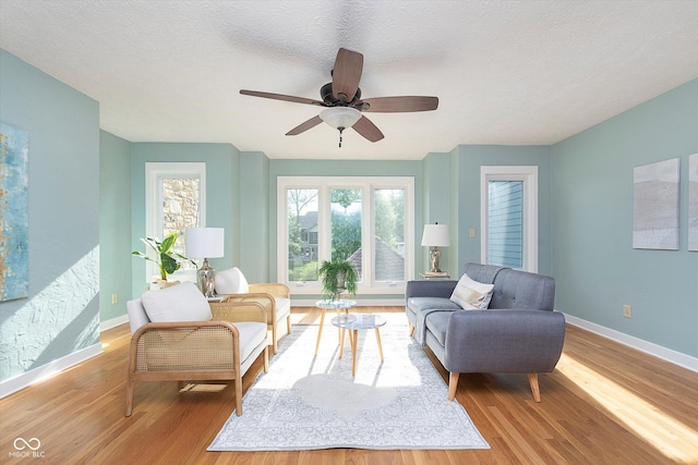 living area featuring a ceiling fan, a textured ceiling, baseboards, and wood finished floors