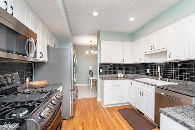 kitchen featuring stainless steel appliances, a sink, white cabinetry, light wood finished floors, and an inviting chandelier