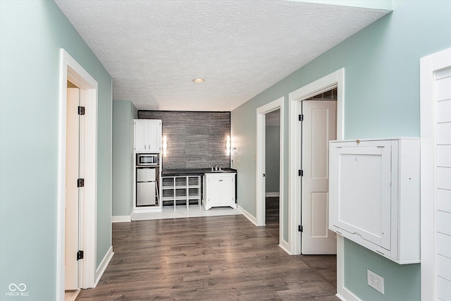 hall with dark wood-type flooring, an accent wall, a textured ceiling, and baseboards