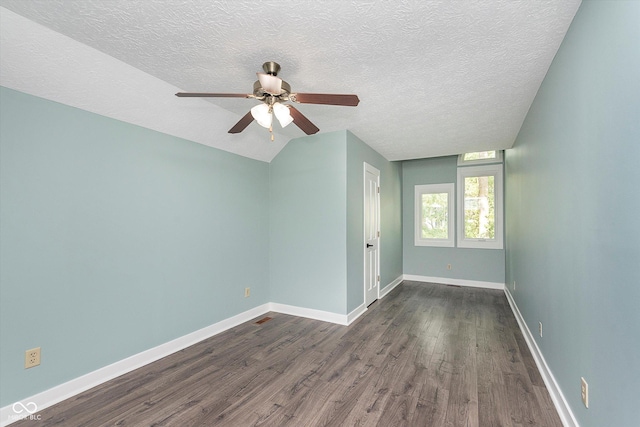 empty room featuring dark wood-type flooring, vaulted ceiling, a textured ceiling, ceiling fan, and baseboards