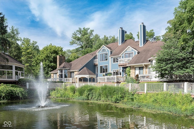 back of house featuring a water view, fence, and a chimney