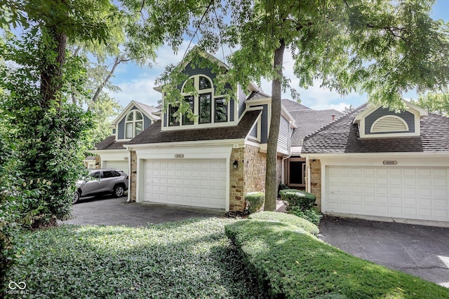 view of front of property featuring a garage, stone siding, a shingled roof, and driveway