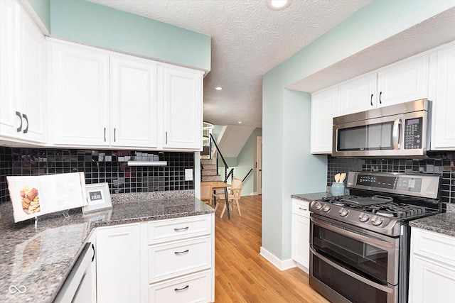 kitchen with stainless steel appliances, white cabinets, light wood-style floors, tasteful backsplash, and dark stone countertops