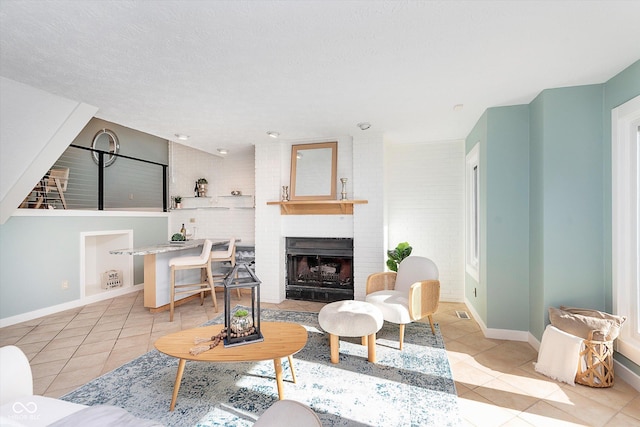 tiled living room with a textured ceiling, a brick fireplace, and baseboards