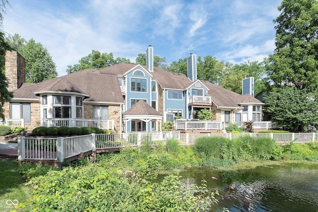 back of house with stone siding, a water view, fence, and a chimney