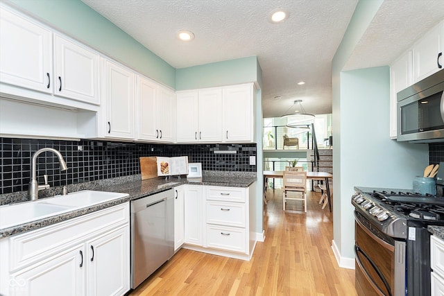 kitchen featuring white cabinets, decorative backsplash, light wood-style flooring, stainless steel appliances, and a sink