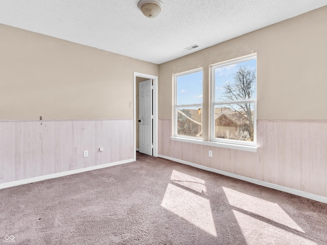 carpeted spare room featuring a wainscoted wall, a textured ceiling, and visible vents