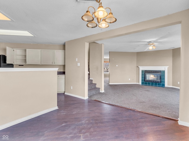 unfurnished living room with ceiling fan with notable chandelier, dark wood-style flooring, a fireplace, and baseboards