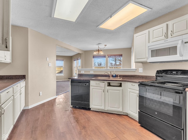 kitchen featuring a peninsula, a sink, light wood-style floors, white cabinets, and black appliances