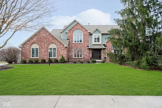 traditional home with a front yard, brick siding, and roof with shingles