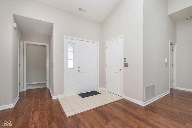 foyer entrance featuring a high ceiling, wood finished floors, visible vents, and baseboards