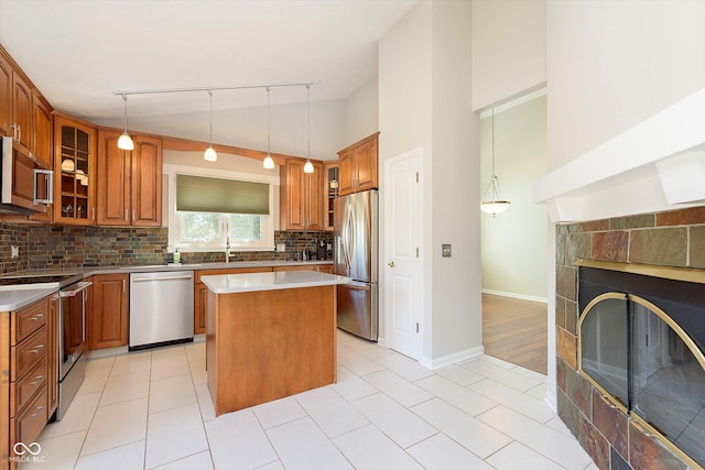 kitchen featuring backsplash, a center island, glass insert cabinets, brown cabinets, and appliances with stainless steel finishes