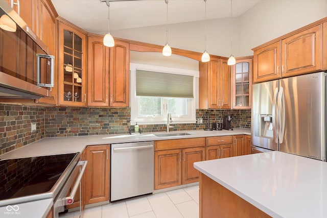 kitchen with pendant lighting, a sink, stainless steel appliances, brown cabinetry, and decorative backsplash