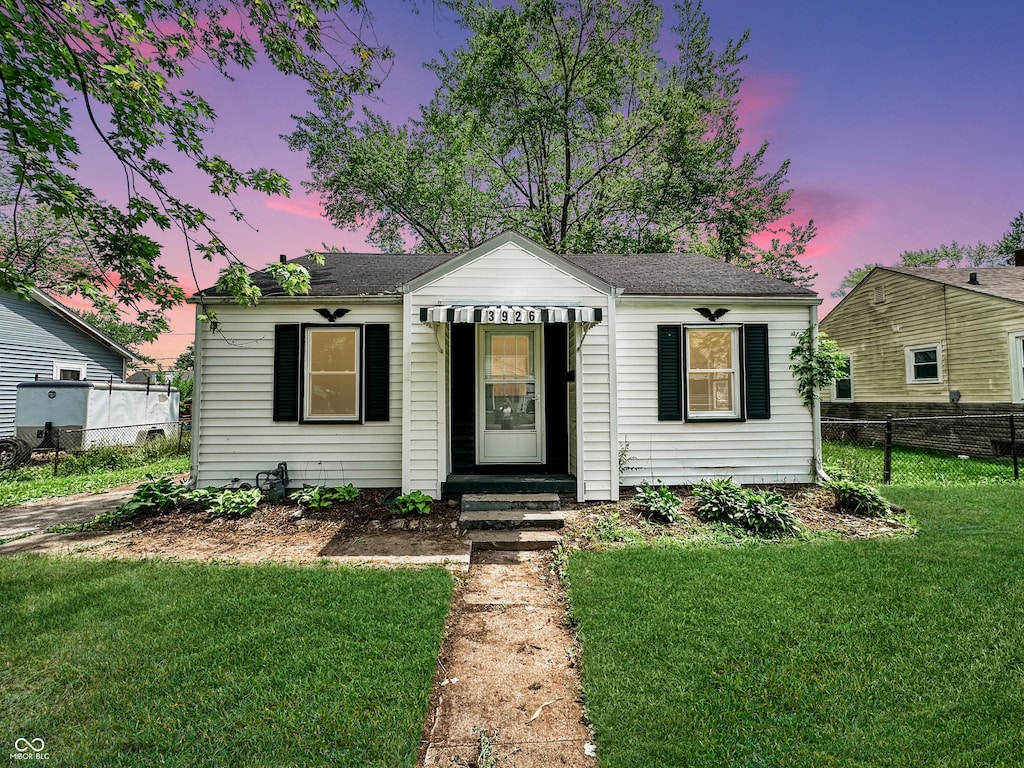 bungalow-style home with entry steps, fence, and a front lawn