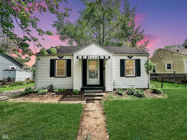 bungalow-style home with entry steps, fence, and a front lawn