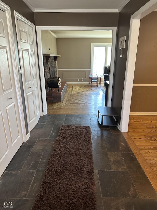 hall featuring a wainscoted wall, crown molding, and stone tile flooring