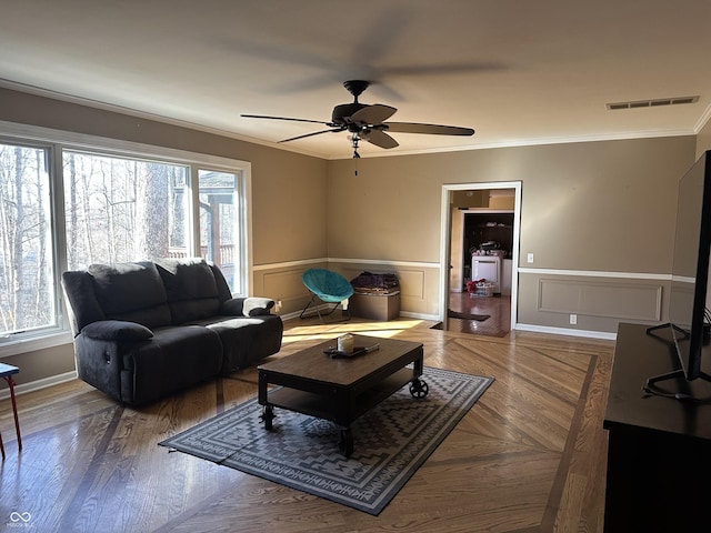 living room featuring a wainscoted wall, ornamental molding, plenty of natural light, and visible vents