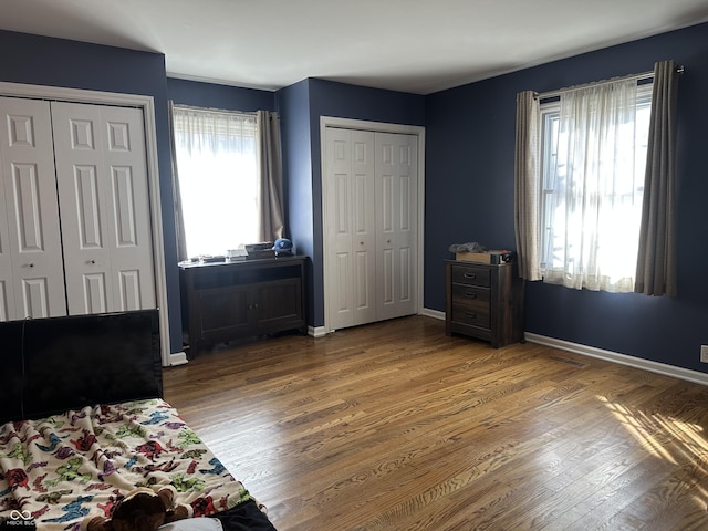 bedroom featuring multiple closets, baseboards, and wood finished floors