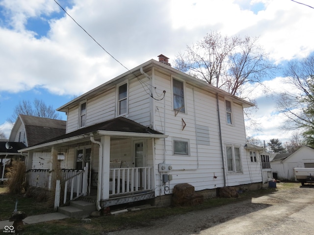 view of front facade featuring covered porch and a chimney