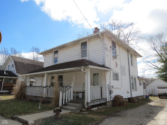 view of front of house featuring a chimney, a porch, and an outbuilding