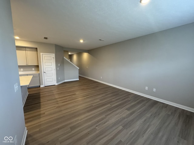 unfurnished living room featuring stairs, baseboards, and dark wood finished floors