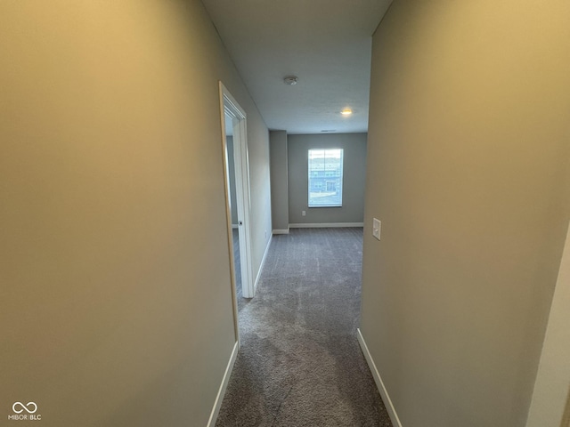 hall featuring dark carpet and baseboards