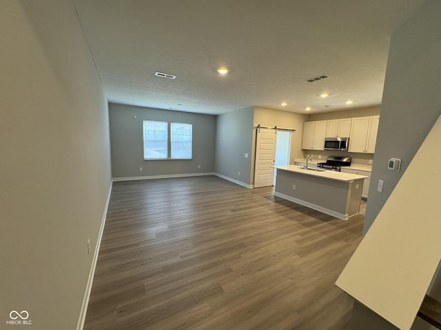 kitchen featuring a barn door, a sink, appliances with stainless steel finishes, dark wood-style floors, and an island with sink