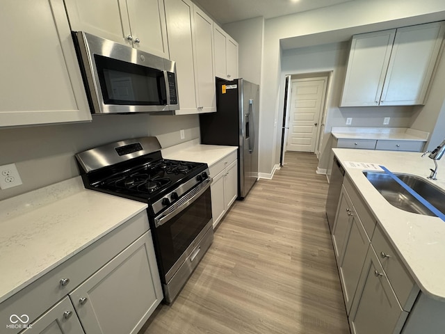 kitchen featuring baseboards, light wood-style flooring, appliances with stainless steel finishes, gray cabinets, and a sink