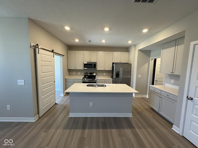 kitchen with stainless steel appliances, a barn door, dark wood-type flooring, and a kitchen island with sink