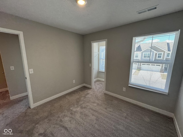 empty room featuring a textured ceiling, carpet flooring, visible vents, and baseboards