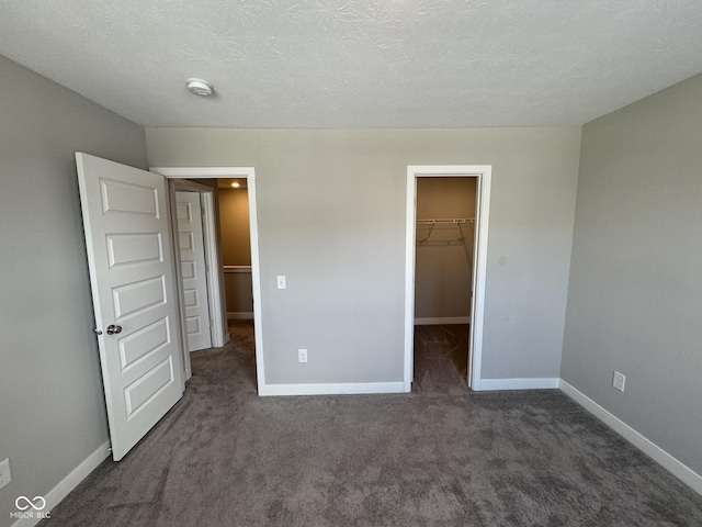 unfurnished bedroom featuring carpet, a spacious closet, baseboards, and a textured ceiling