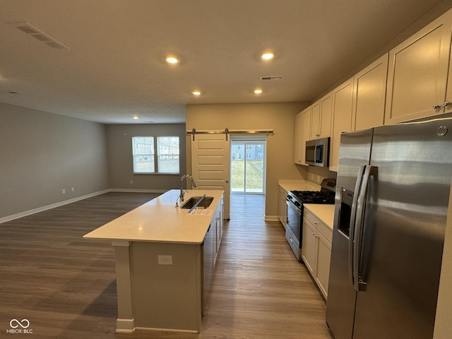 kitchen featuring a barn door, a center island with sink, visible vents, stainless steel appliances, and a sink