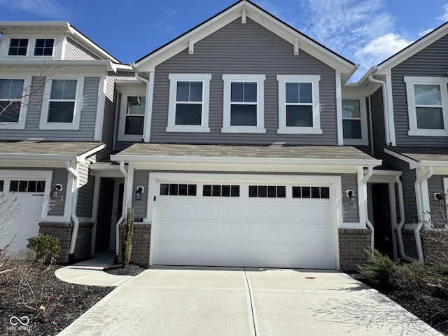 townhome / multi-family property with driveway, an attached garage, a shingled roof, and brick siding