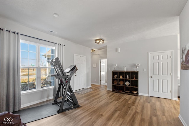 workout area with baseboards, plenty of natural light, visible vents, and wood finished floors