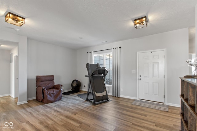 exercise room with a textured ceiling, baseboards, and wood finished floors