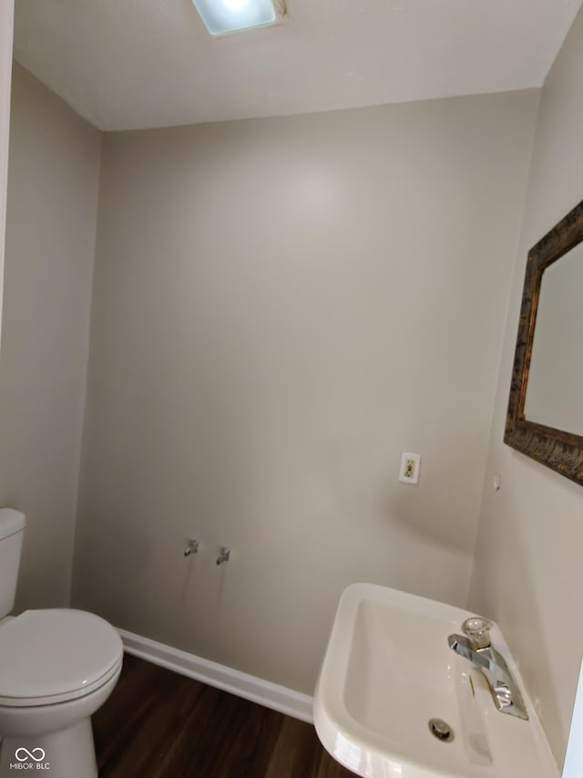 half bathroom featuring baseboards, a sink, toilet, and wood finished floors