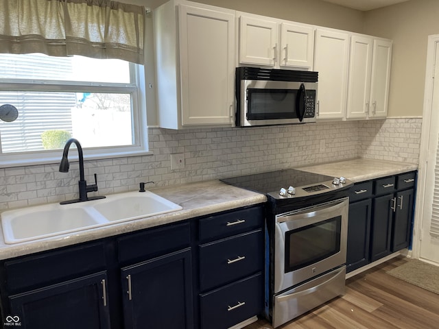 kitchen with appliances with stainless steel finishes, wood finished floors, a sink, white cabinetry, and backsplash