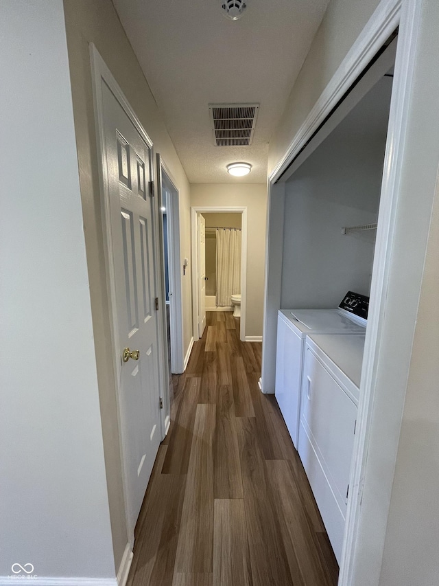 hallway featuring dark wood-type flooring, washer and dryer, visible vents, and baseboards