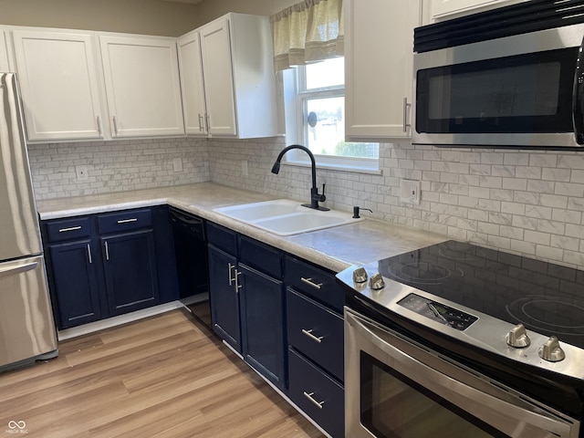 kitchen featuring light wood-style flooring, appliances with stainless steel finishes, blue cabinets, white cabinetry, and a sink