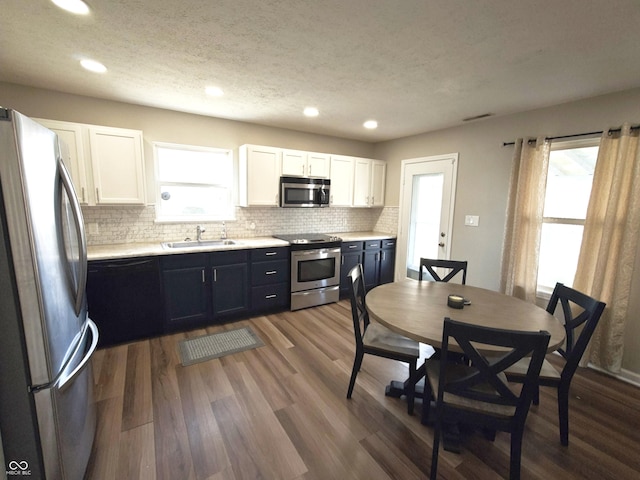 kitchen featuring decorative backsplash, dark wood-style floors, stainless steel appliances, white cabinetry, and a sink