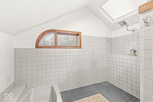 bathroom featuring vaulted ceiling with skylight, a tile shower, and a textured ceiling