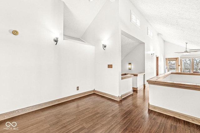 spare room with baseboards, ceiling fan, dark wood-type flooring, vaulted ceiling, and a textured ceiling